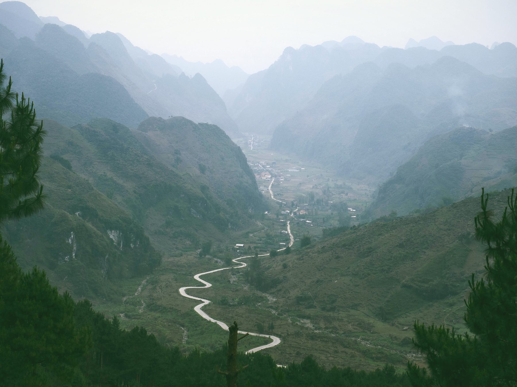 A narrow road winding through a misty green valley between mountains