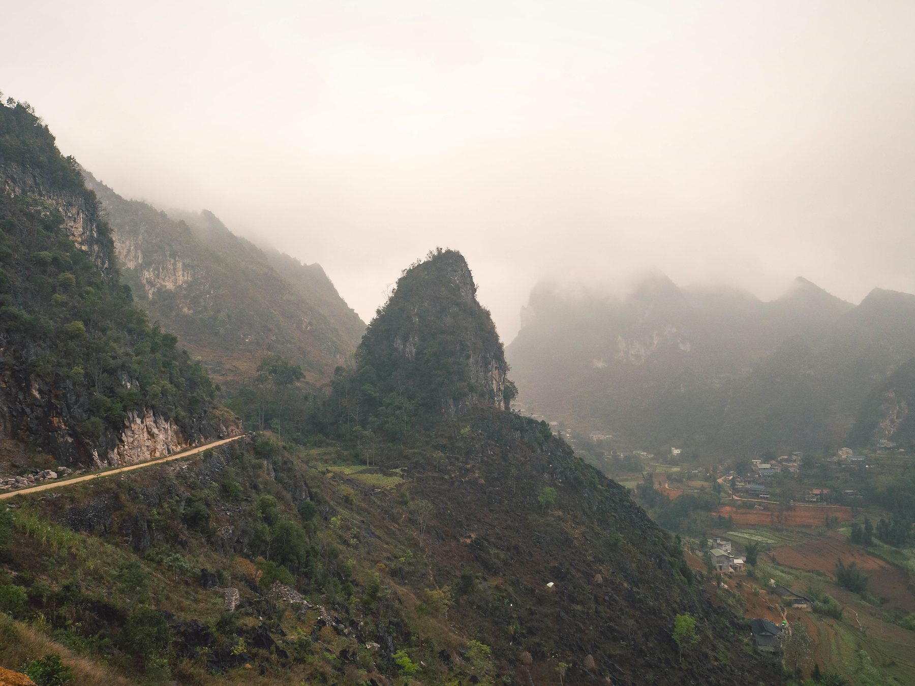 A pointed rock peak rising from fog-covered hills beside a mountain road